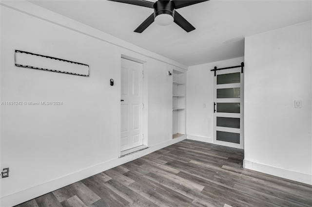 unfurnished room featuring baseboards, a ceiling fan, a barn door, and wood finished floors