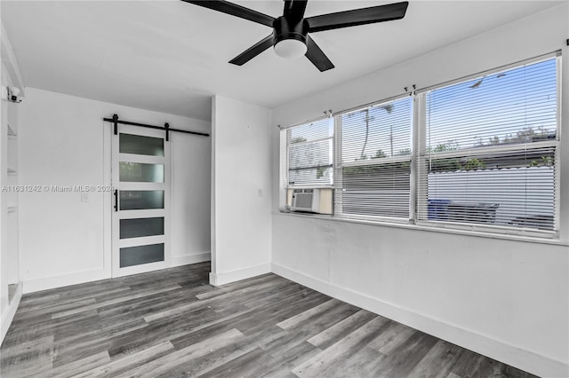 empty room featuring cooling unit, wood finished floors, baseboards, ceiling fan, and a barn door