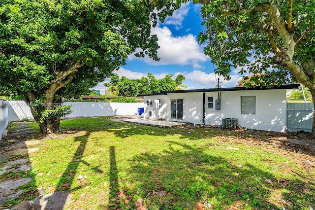 rear view of property featuring central air condition unit, a lawn, a fenced backyard, and stucco siding