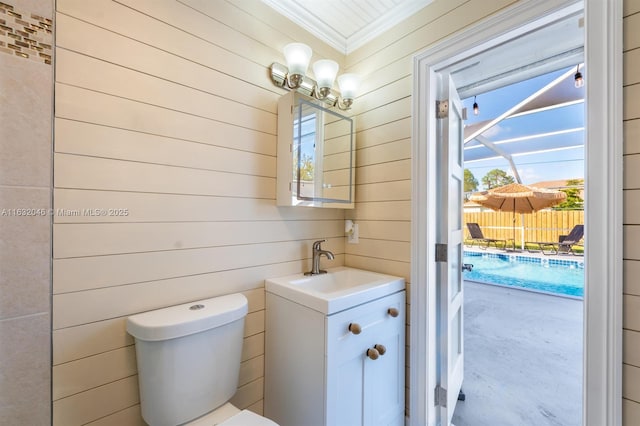 bathroom with toilet, wooden walls, crown molding, and vanity