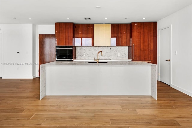 kitchen featuring an island with sink, tasteful backsplash, light hardwood / wood-style floors, and sink