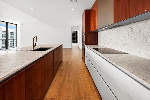 kitchen with sink, wall chimney exhaust hood, light hardwood / wood-style floors, decorative backsplash, and black electric stovetop