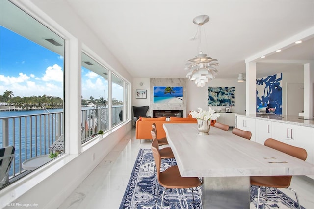 dining area with a water view, a high end fireplace, and a notable chandelier