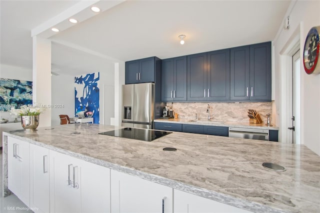 kitchen with stainless steel appliances, light stone counters, blue cabinets, sink, and tasteful backsplash