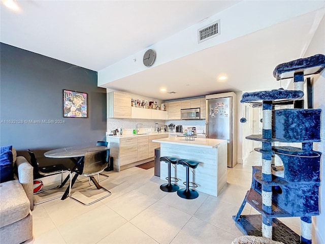 kitchen with light tile patterned flooring, a breakfast bar area, light brown cabinetry, and a kitchen island