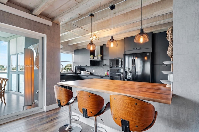 kitchen with dark wood-type flooring, black appliances, a kitchen breakfast bar, wall chimney range hood, and hanging light fixtures