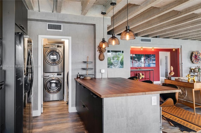 kitchen featuring butcher block counters, dark wood-type flooring, hanging light fixtures, stacked washer / dryer, and stainless steel fridge