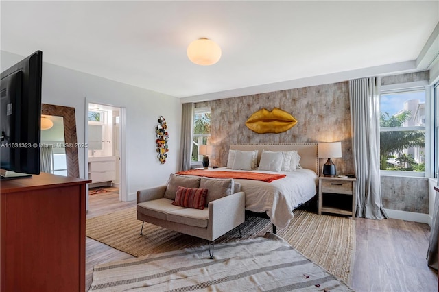 bedroom with light wood-type flooring, ensuite bath, and multiple windows