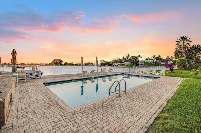 pool at dusk featuring a water view and a patio