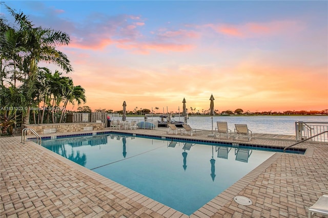 pool at dusk featuring a patio and a water view