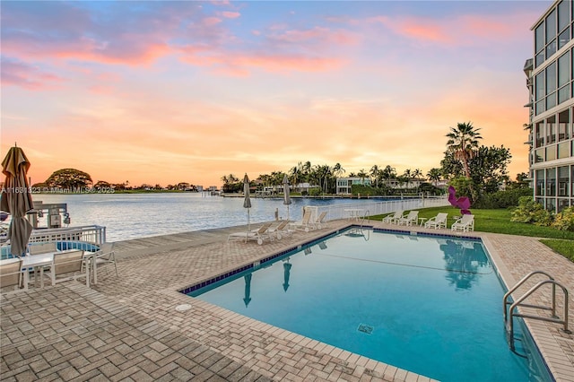 pool at dusk featuring a patio and a water view