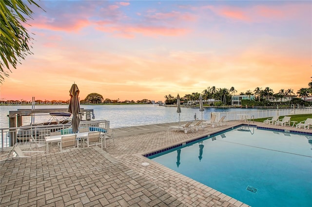 pool at dusk featuring a patio and a water view