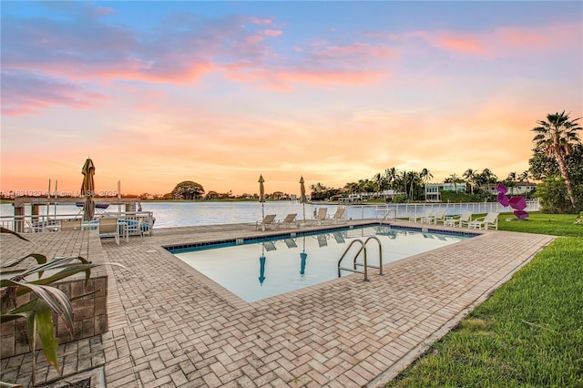 pool at dusk featuring a water view and a patio area