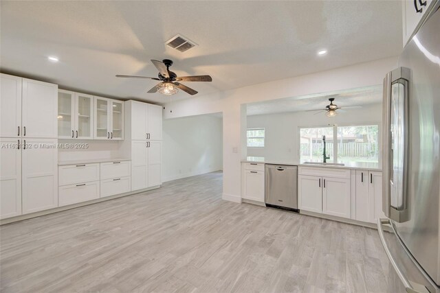 kitchen with ceiling fan, sink, light wood-type flooring, appliances with stainless steel finishes, and white cabinets