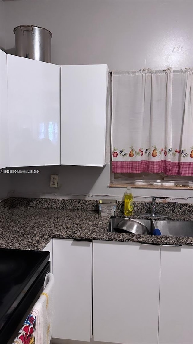 kitchen featuring range, white cabinetry, dark stone countertops, and sink