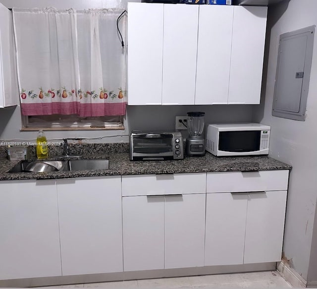 kitchen with dark stone countertops, white cabinetry, sink, and electric panel