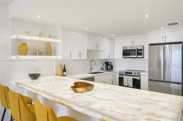 kitchen featuring sink, appliances with stainless steel finishes, a breakfast bar area, kitchen peninsula, and white cabinets