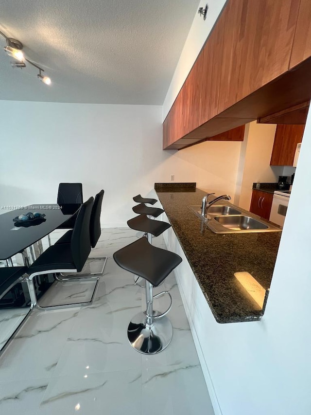 kitchen with rail lighting, sink, dark stone countertops, a breakfast bar area, and a textured ceiling