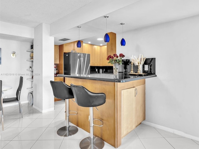 kitchen with decorative light fixtures, kitchen peninsula, stainless steel fridge, light tile patterned floors, and a kitchen breakfast bar