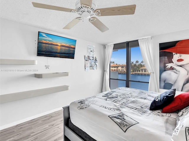 bedroom featuring a textured ceiling, a water view, access to outside, ceiling fan, and hardwood / wood-style flooring