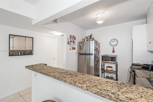 kitchen with dark stone countertops, kitchen peninsula, light tile patterned flooring, and stainless steel appliances