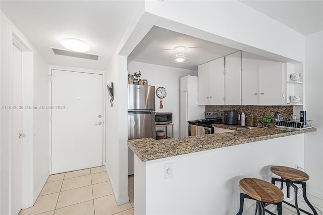 kitchen featuring light tile patterned flooring, white cabinetry, tasteful backsplash, kitchen peninsula, and stainless steel appliances