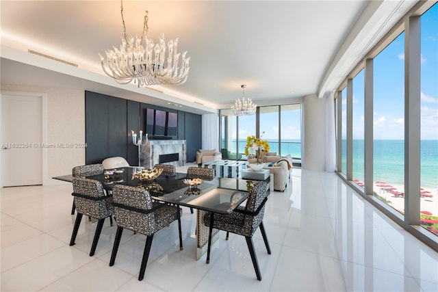 tiled dining room with a view of the beach, floor to ceiling windows, a water view, an inviting chandelier, and a fireplace