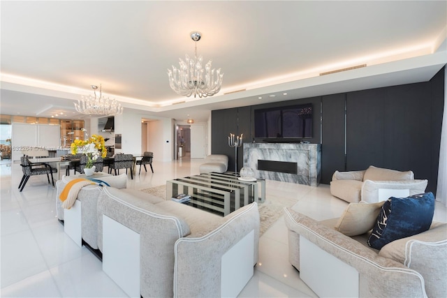 living room featuring light tile patterned flooring, a premium fireplace, a raised ceiling, and a notable chandelier