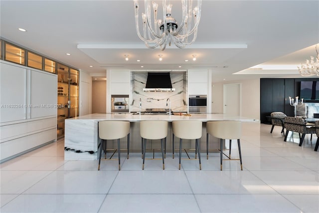 kitchen with decorative light fixtures, range hood, white cabinetry, a large island, and an inviting chandelier