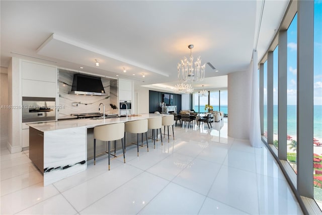 kitchen with premium range hood, a water view, white cabinets, and a spacious island