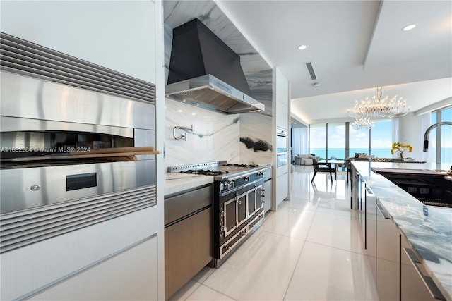 kitchen featuring stove, a water view, light stone counters, tasteful backsplash, and wall chimney exhaust hood