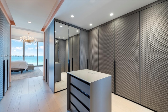 hallway featuring a water view, a chandelier, light wood-type flooring, and a wall of windows