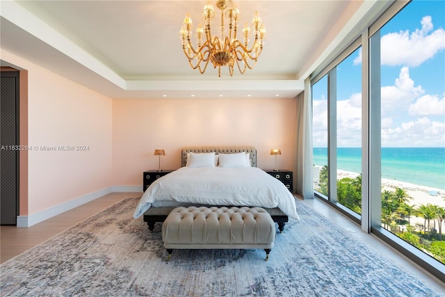 bedroom with multiple windows, a water view, a tray ceiling, and a view of the beach