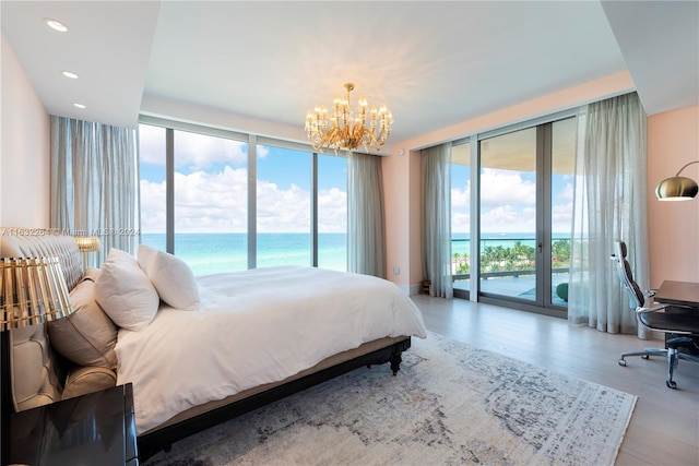 bedroom with multiple windows, access to exterior, light hardwood / wood-style flooring, and a water view