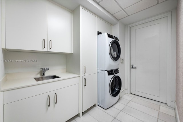 laundry area featuring sink, light tile patterned floors, cabinets, and stacked washer and clothes dryer