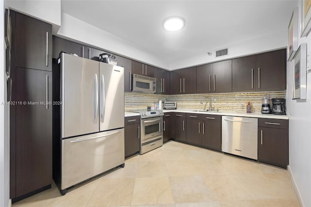 kitchen with dark brown cabinets, light tile patterned floors, appliances with stainless steel finishes, decorative backsplash, and sink