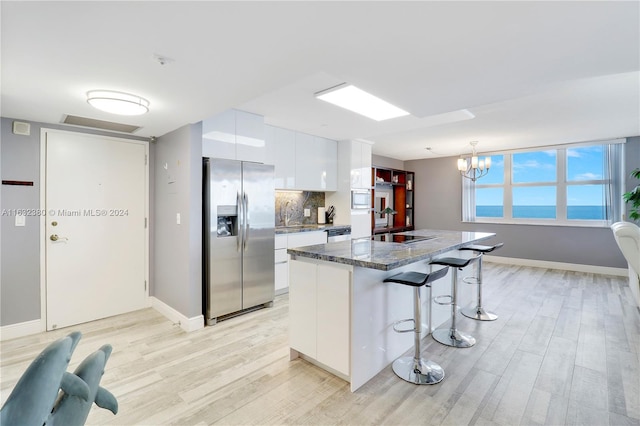 kitchen featuring white cabinetry, pendant lighting, stainless steel fridge with ice dispenser, dark stone countertops, and light hardwood / wood-style flooring