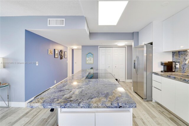 kitchen with stainless steel fridge, white cabinetry, dark stone countertops, and light hardwood / wood-style floors