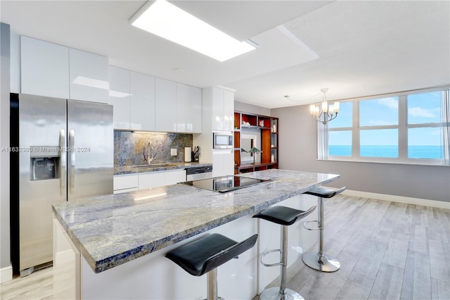 kitchen with a water view, a kitchen breakfast bar, stainless steel appliances, white cabinets, and decorative light fixtures