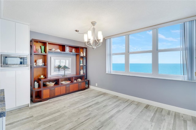 dining area with light hardwood / wood-style floors, a water view, a textured ceiling, and an inviting chandelier