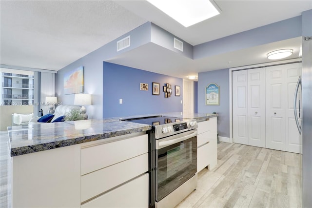 kitchen with appliances with stainless steel finishes, light hardwood / wood-style floors, a textured ceiling, dark stone countertops, and white cabinetry