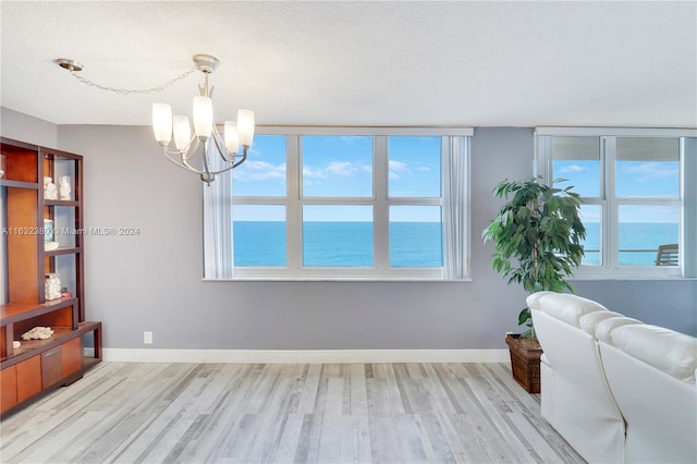 dining space with light hardwood / wood-style floors, a notable chandelier, a water view, and a textured ceiling