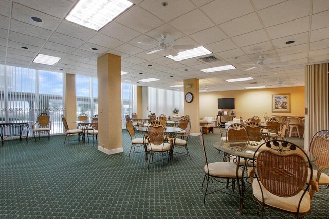 carpeted dining area with a wall of windows, ceiling fan, and a paneled ceiling