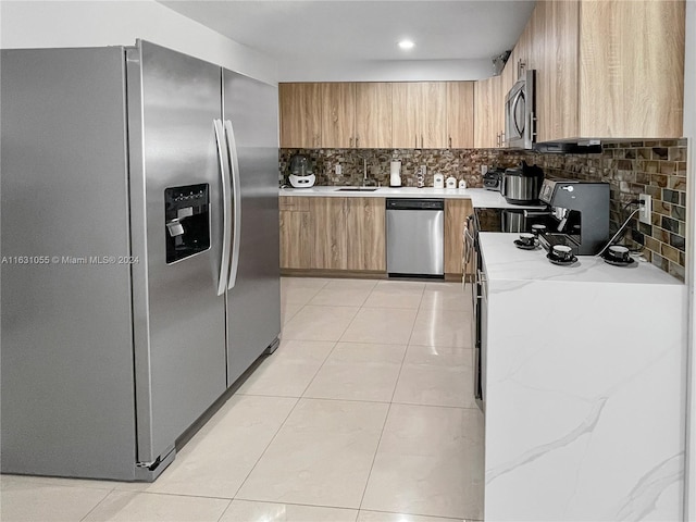 kitchen featuring tasteful backsplash, stainless steel appliances, sink, light stone countertops, and light tile patterned floors