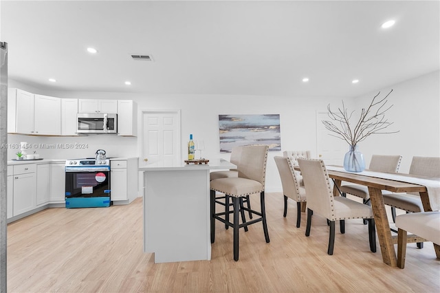 kitchen with electric stove, a kitchen breakfast bar, white cabinetry, light hardwood / wood-style floors, and a center island