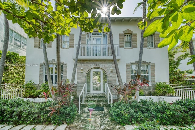 view of front of property featuring a balcony, fence, stone siding, and stucco siding