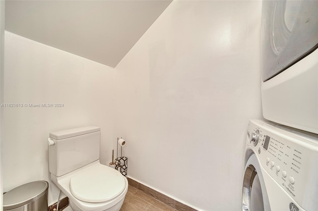 bathroom with toilet, stacked washer and clothes dryer, and wood-type flooring