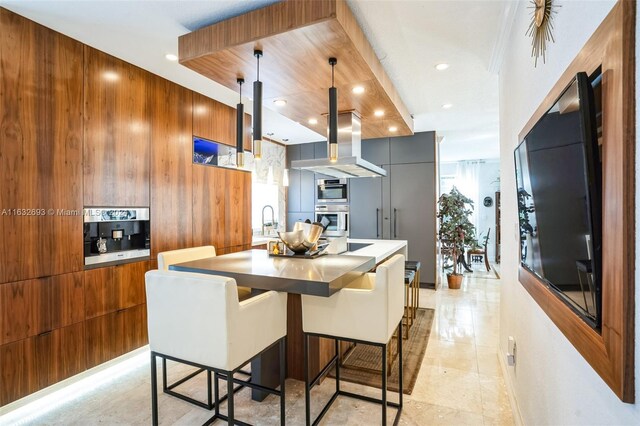 kitchen featuring hanging light fixtures, a kitchen island, island range hood, wooden walls, and a breakfast bar