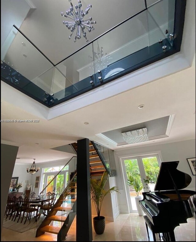 stairs featuring a notable chandelier, a raised ceiling, and a healthy amount of sunlight