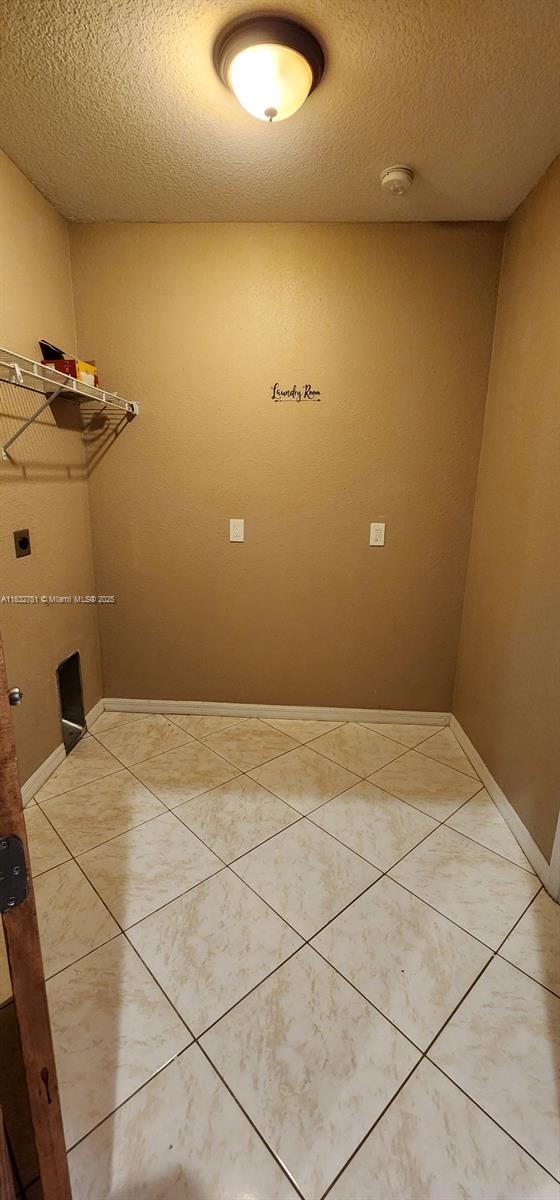 laundry area featuring a textured ceiling, tile patterned floors, and electric dryer hookup